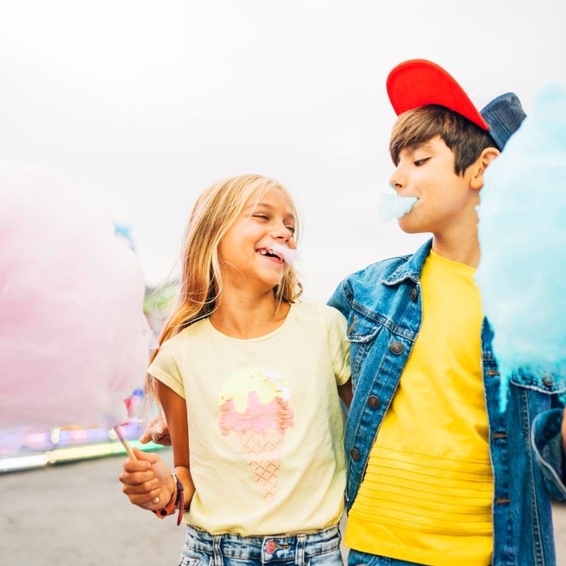 Boy and girl eating sweet cotton at the amusement park